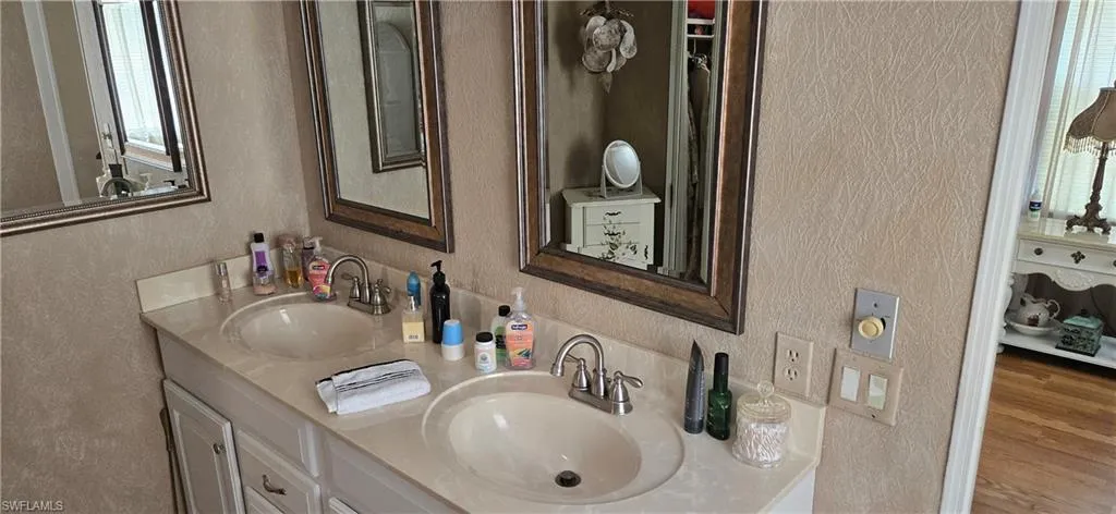 Full bathroom with a textured wall, double vanity, and wood finished floors