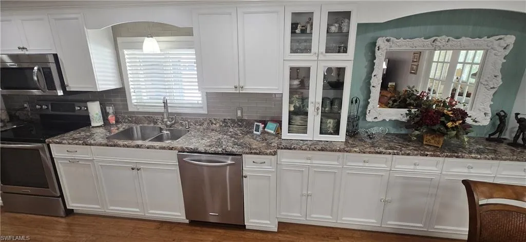 Kitchen featuring appliances with stainless steel finishes, white cabinets, decorative backsplash, dark stone countertops, and dark wood-style floors
