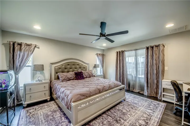 Dark wood-finish flooring with a ceiling fan, recessed lighting, and multiple windows