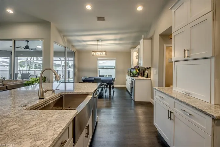 Kitchen island with an undermount stainless steel sink and gooseneck faucet, light-colored stone-finish countertops, white shaker-style cabinetry, and dark wood-finish flooring