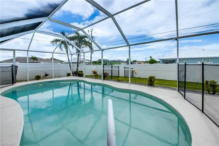 Screened enclosure featuring a freeform swimming pool, surrounding concrete decking, perimeter fencing, and a separate pool safety barrier