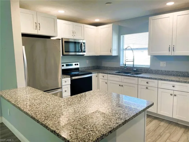 Kitchen featuring stainless steel appliances, light stone counters, white cabinets, and recessed lighting