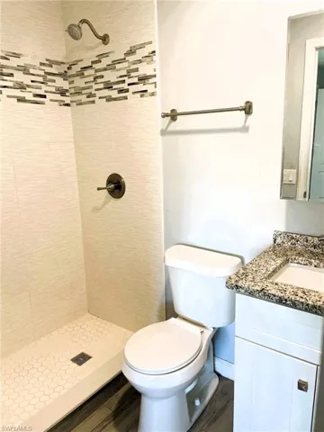 Full bath featuring a shower stall, vanity, and dark wood-style flooring
