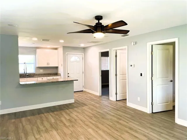 Kitchen featuring white cabinets, dark stone countertops, a ceiling fan, light wood finished floors, and a peninsula