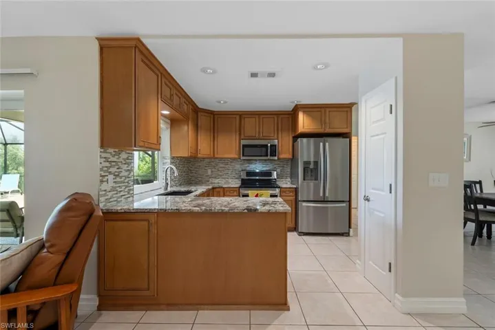 Kitchen with sink, kitchen peninsula, stone counters, appliances with stainless steel finishes, and light tile patterned floors