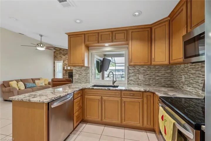 Kitchen with sink, vaulted ceiling, kitchen peninsula, stainless steel appliances, and light tile patterned floors