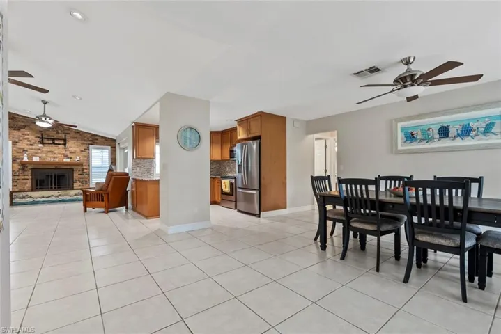 Dining space featuring ceiling fan, light tile patterned flooring, a fireplace, and vaulted ceiling