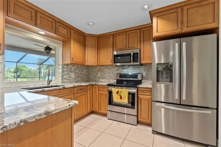 Kitchen with tasteful backsplash, sink, stainless steel appliances, light tile patterned floors, and light stone countertops