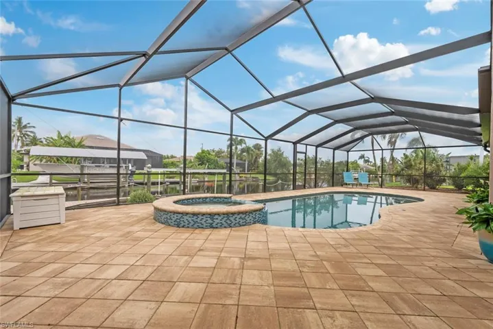 View of pool featuring a patio, glass enclosure, and an in ground hot tub