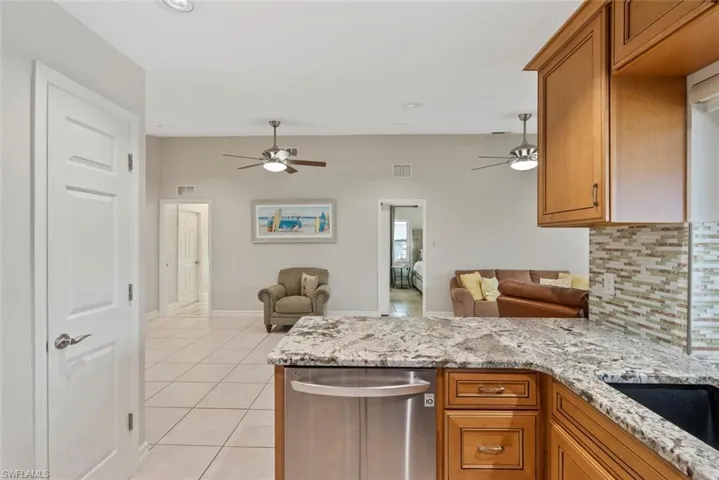 Kitchen with decorative backsplash, light stone counters, kitchen peninsula, light tile patterned floors, and ceiling fan