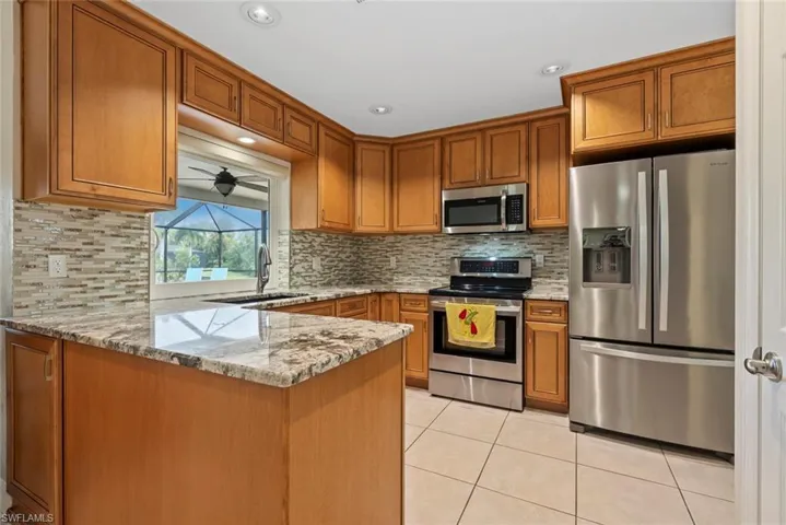 Kitchen with light stone counters, sink, kitchen peninsula, decorative backsplash, and stainless steel appliances