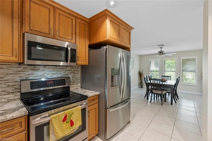 Kitchen with ceiling fan, stainless steel appliances, light tile patterned floors, and decorative backsplash