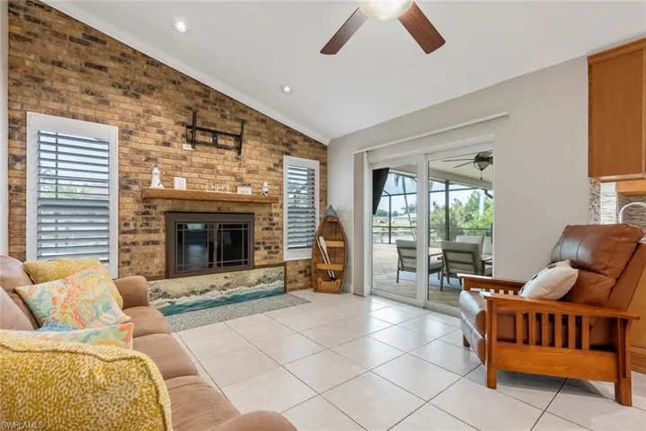 Tiled living room featuring vaulted ceiling, brick wall, a fireplace, ceiling fan, and ornamental molding