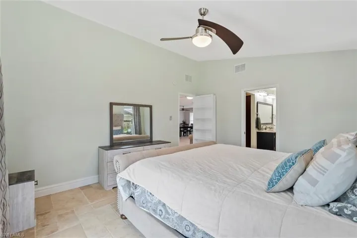 Bedroom featuring ceiling fan, lofted ceiling, and ensuite bath