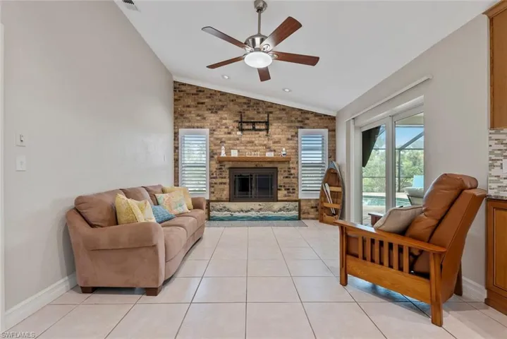 Tiled living room featuring a fireplace, vaulted ceiling, and ceiling fan