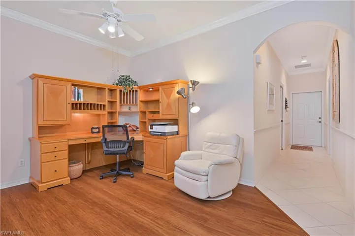 Home office with crown molding, arched walkways, a ceiling fan, and light wood-style floors
