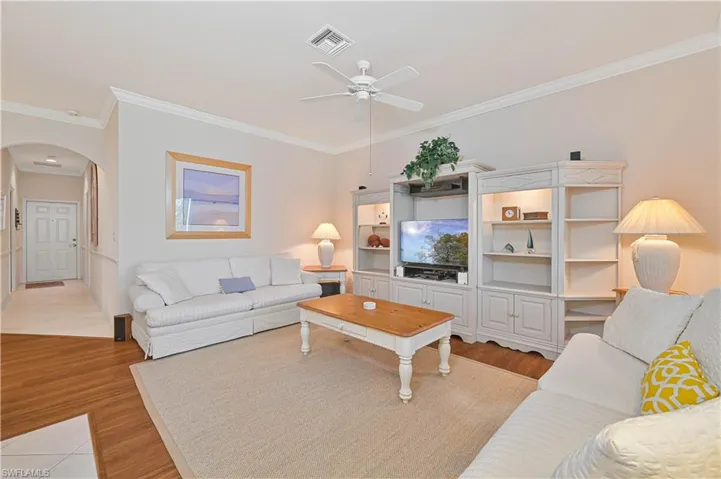 Living area with arched walkways, crown molding, light wood-style flooring, and ceiling fan
