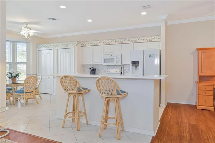 Kitchen featuring light countertops, white appliances, tasteful backsplash, crown molding, and a kitchen bar