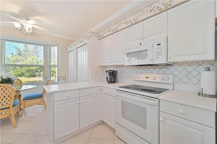 Kitchen featuring white appliances, light countertops, ornamental molding, white cabinets, and a peninsula