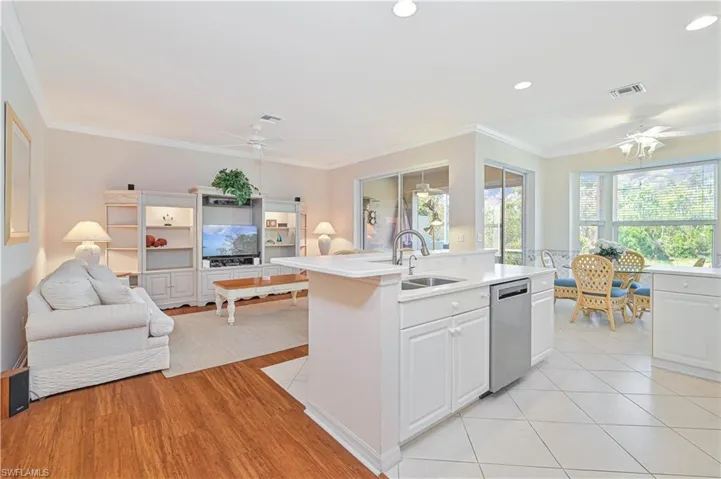 Kitchen with ceiling fan, open floor plan, a kitchen island with sink, crown molding, and white cabinets