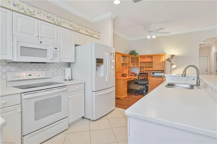 Kitchen with white appliances, light countertops, white cabinets, ornamental molding, and arched walkways