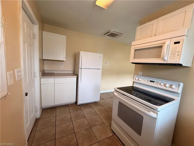 Kitchen with white appliances, white cabinets, light countertops, and dark tile patterned floors