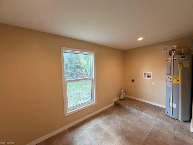 Laundry area with electric water heater, hookup for an electric dryer, hookup for a washing machine, recessed lighting, and light tile patterned floors