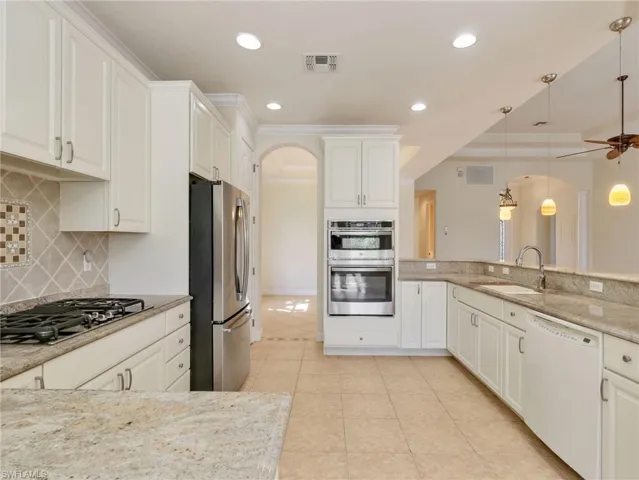 Kitchen with white cabinetry, stainless steel appliances, light stone counters, arched walkways, and ornamental molding