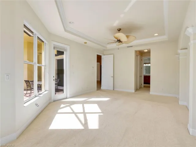 Unfurnished bedroom featuring light colored carpet, ensuite bathroom, a ceiling fan, a raised ceiling, and crown molding