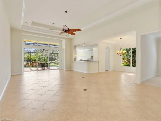 Unfurnished living room featuring a sunroom, ceiling fan, plenty of natural light, a raised ceiling, and a chandelier