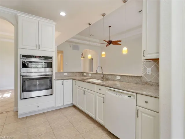 Kitchen with a tray ceiling, dishwasher, stainless steel double oven, white cabinets, and light stone counters