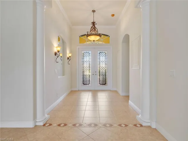 Foyer entrance with decorative columns, french doors, ornamental molding, light tile patterned floors, and arched walkways