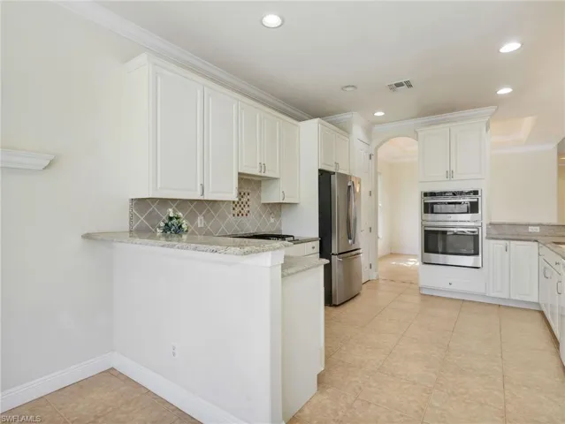 Kitchen with a peninsula, white cabinetry, light stone countertops, arched walkways, and crown molding