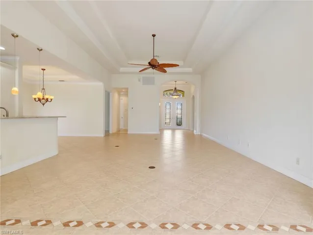 Unfurnished living room with a raised ceiling, arched walkways, ceiling fan, and a chandelier