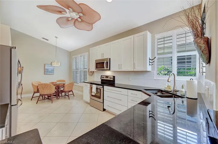 Kitchen featuring white cabinets, stainless steel appliances, lofted ceiling, a sink, and light tile patterned floors