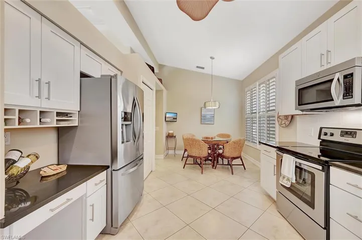 Kitchen featuring light tile patterned flooring, backsplash, white cabinetry, appliances with stainless steel finishes, and dark countertops