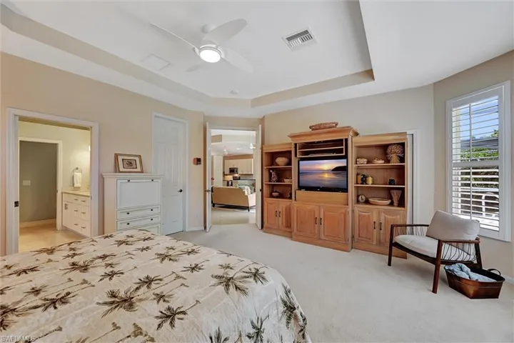 Bedroom with a tray ceiling, ensuite bath, light colored carpet, and ceiling fan