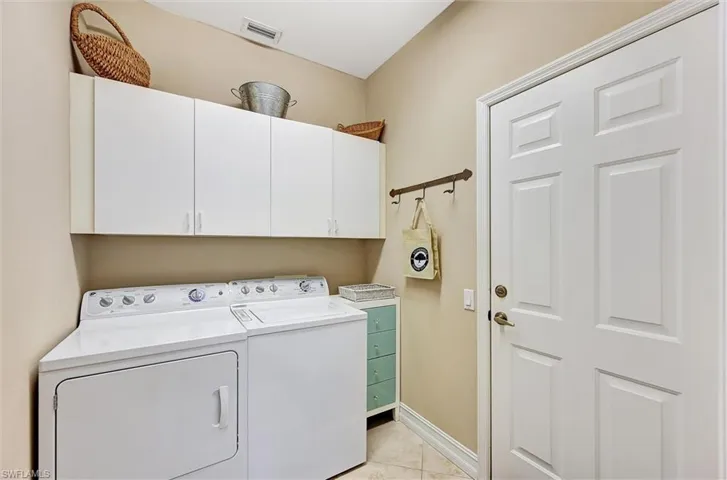 Laundry area featuring light tile patterned floors, baseboards, washer and dryer, and cabinet space