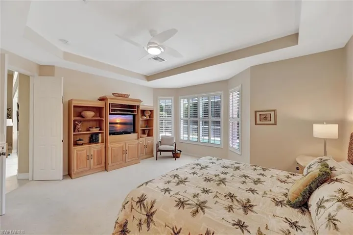 Bedroom with baseboards, a raised ceiling, visible vents, a ceiling fan, and light carpet