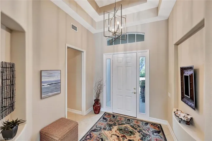 Tiled entryway with a tray ceiling, baseboards, a chandelier, a towering ceiling.