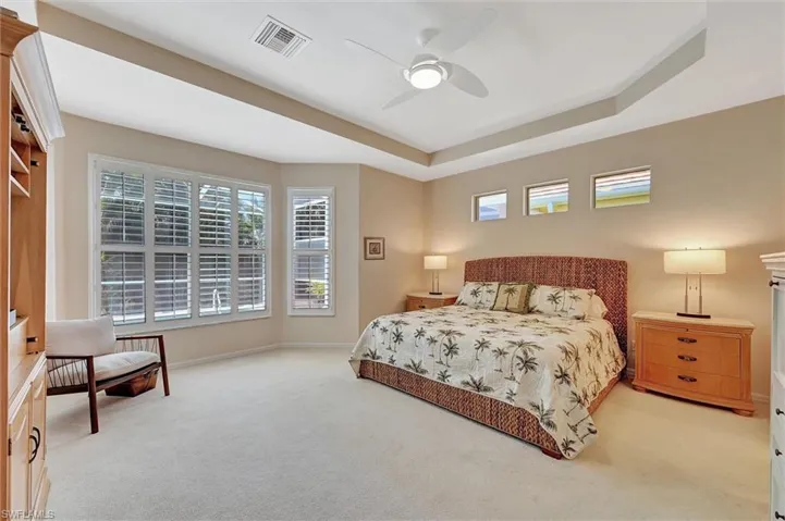 Bedroom with a tray ceiling, light colored carpet, baseboards, ceiling fan.