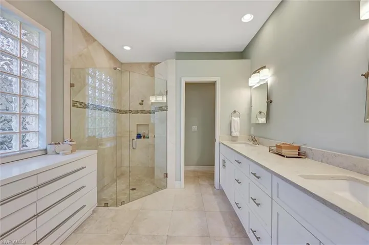 Bathroom with double vanity, a sink, a stall shower, and recessed lighting