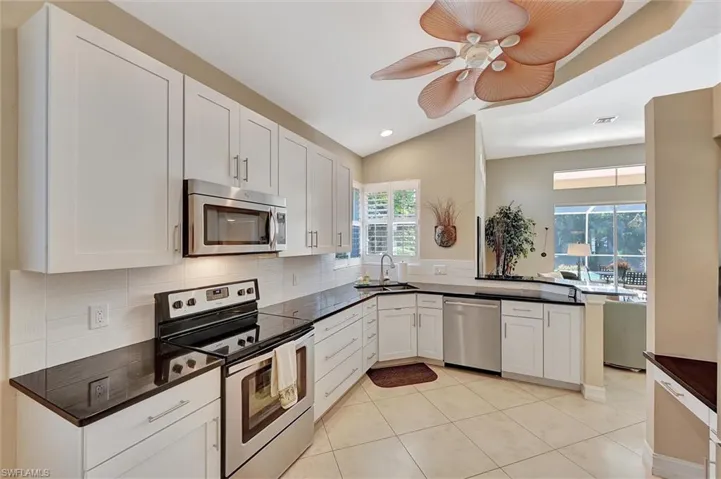 Kitchen featuring a sink, backsplash, white cabinetry, appliances with stainless steel finishes, and dark countertops