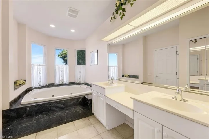 Full bath with a whirlpool tub, double vanity, light tile patterned floors, and recessed lighting