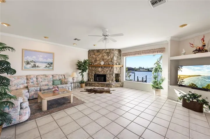 Living room with crown molding, a stone fireplace, ceiling fan, and tile patterned floors