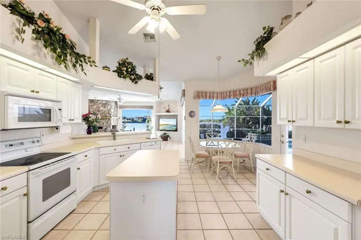 Kitchen with white appliances, a ceiling fan, light countertops, a kitchen island, and white cabinetry