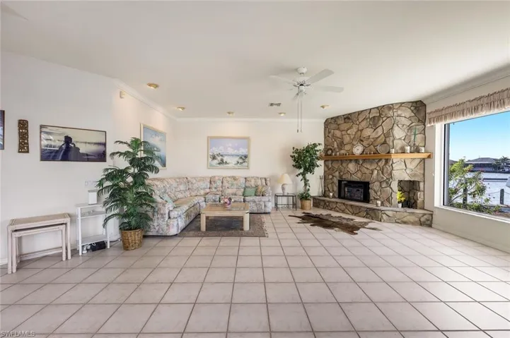 Living room with crown molding, a fireplace, ceiling fan, and light tile patterned flooring