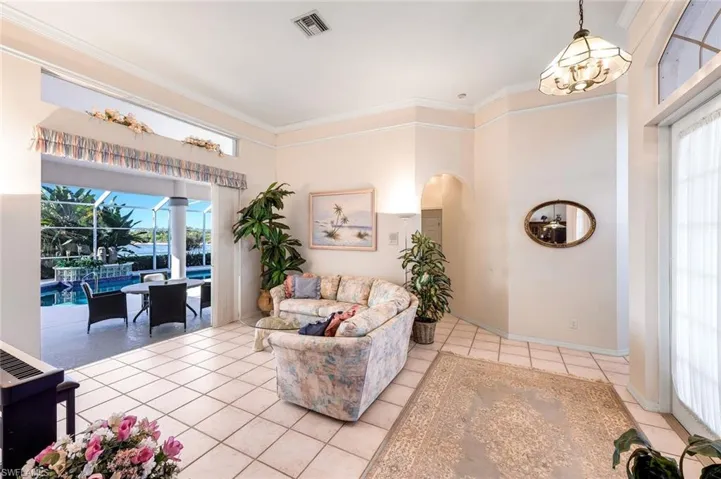 Living area featuring ornamental molding, light tile patterned floors, a chandelier, a sunroom, and arched walkways