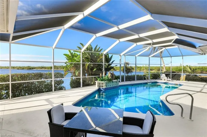Outdoor pool with a sunroom, glass enclosure, a patio, and a water view