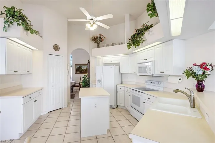 Kitchen with white appliances, light countertops, arched walkways, a kitchen island, and a high ceiling